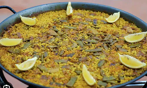 Classic vegetable paella in metal pan topped with fresh lemon wedges and green bean strips at La Paella, a Spanish Restaurant in Sugar Land