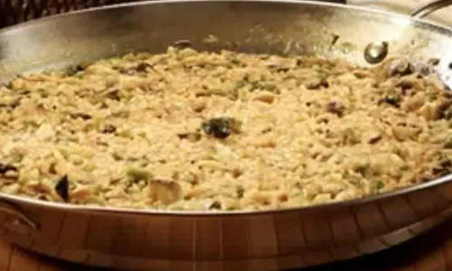 Creamy mushroom risotto cooked inside large round metal paella pan resting on wooden trivet at La Paella, a Spanish Restaurant in Sugar Land