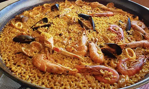 Seafood paella loaded with large shrimp, mussels, clams and squid over saffron yellow rice in wide pan at La Paella, a Spanish Restaurant in Sugar Land