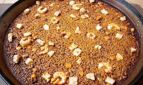 Dark seafood paella with shrimp and white fish chunks mixed in rich brown saffron rice inside metal pan at La Paella, a Spanish Restaurant in Sugar Land