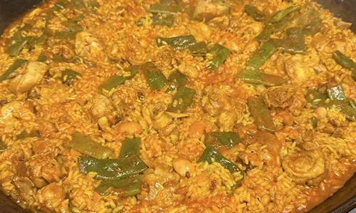 Chicken vegetable paella with tender poultry pieces and sliced green bell peppers over golden saffron rice pan at La Paella, a Spanish Restaurant in Sugar Land