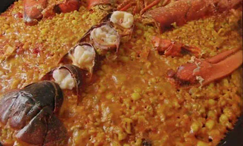 Lobster paella featuring split red lobster tails resting atop vibrant saffron-infused Spanish rice in metal pan at La Paella, a Spanish Restaurant in Sugar Land Lobster paella featuring split red lobster tails resting atop vibrant saffron-infused Spanish rice in metal pan at La Paella, a Spanish Restaurant in Sugar Land